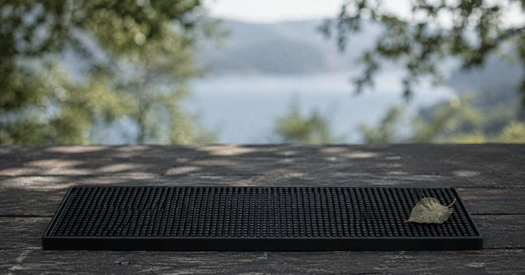 Black rubber bar mat airing outdoors on a weathered timber table with a fallen leaf resting on its edge